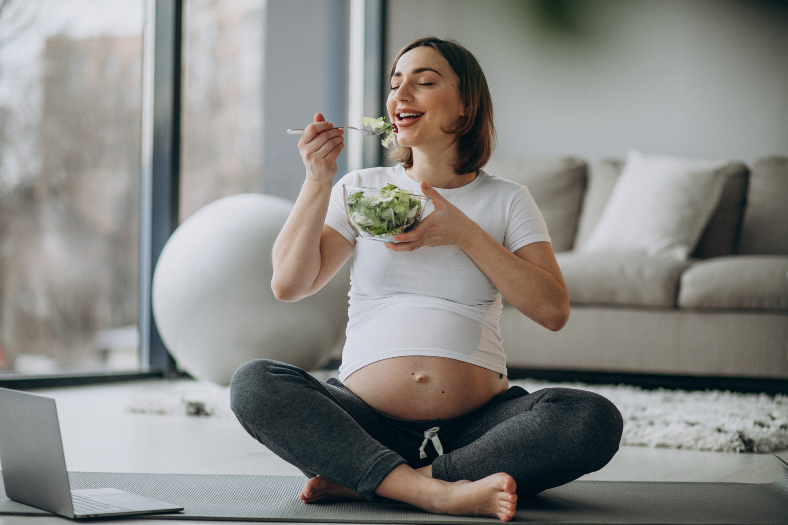 Mulher grávida jovem comendo salada em casa